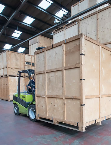 Green Clark forklift moving a large wooden storage crate in a warehouse with stacked wooden containers
