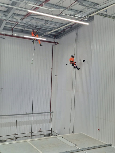 Two abseilers working at height inside a large white industrial warehouse facility in Manchester