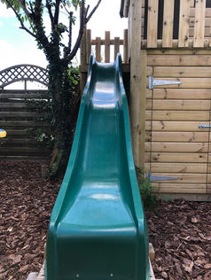 Bright green plastic slide attached to an outdoor wooden play tower