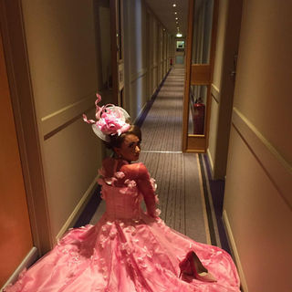 A person in a pink gown with flower sits on a hotel hallway floor