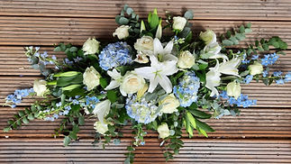Formal blue and white funeral spray with lilies and carnations on a wooden background