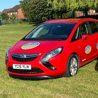 A bright red car is parked on a grassy field with the company branding