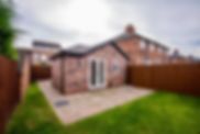 Modern single storey brick building extension with white French doors opening onto a stone paved patio and green lawn