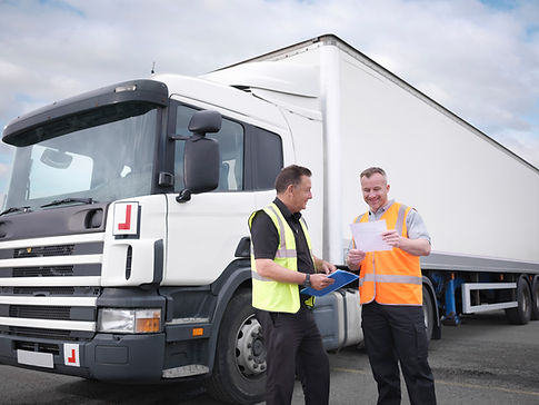 Two men in reflective vests stand beside a white delivery truck, smiling and discussing documents