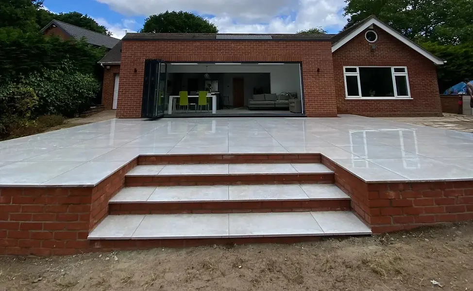 Modern brick house with open glass doors leading to a polished white tile patio