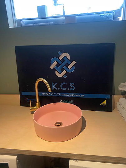 Round pink vessel sink with a gold faucet on a light wood countertop