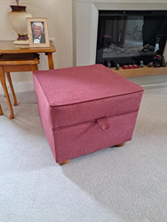 Pink upholstered storage footstool with wooden feet in a living room