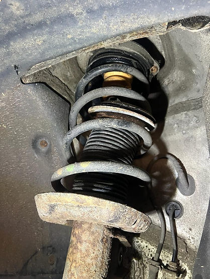 Close-up of a corroded suspension strut and coil spring mounted in a car's wheel arch