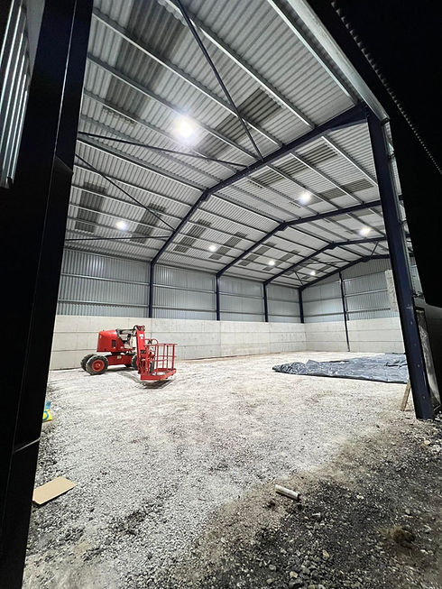 Interior view of a large metal frame industrial shed with a red tractor on a dirt floor