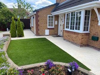 Bright artificial lawn area bordered by stone paving and flower beds
