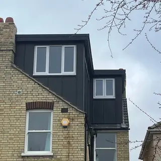 Exterior view of a residential brick house with a large modern dark grey dormer extension