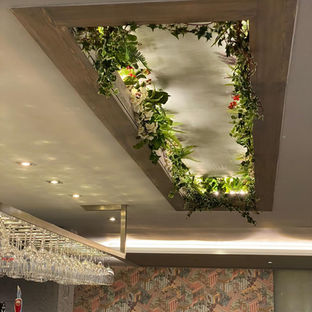 A ceiling feature with a light-up recess surrounded by faux greenery and glasses hanging over a bar area