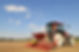 Red tractor pulling a seed drill across a freshly tilled brown field