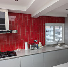 Modern kitchen with grey cabinets bright red brick-style tiles and a window with white shutters