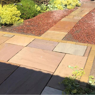 Multicoloured Indian sandstone paving slabs used for a garden path next to decorative bark