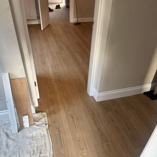 Warm oak laminate flooring planks fitted in a clean residential hallway with white walls