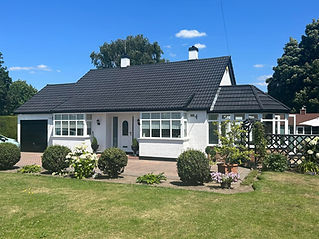 Charming white cottage with a dark grey tiled roof, two large bay windows, and a neat front garden on a sunny day