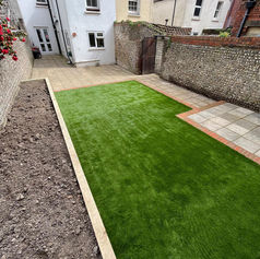 Long, narrow garden with new artificial turf, block paving, and a bordering section of loose soil