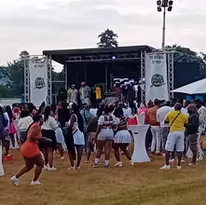 A crowd gathered outdoors in front of a stage with people performing or speaking.