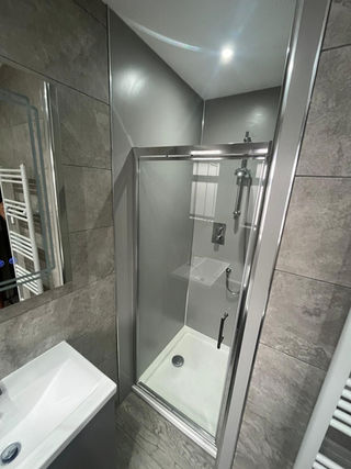Compact grey bathroom with a tiled corner shower enclosure, hinged glass door, and small white vanity