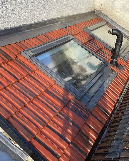Velux skylight fitted into red tile roof with dark lead flashing and vent pipe