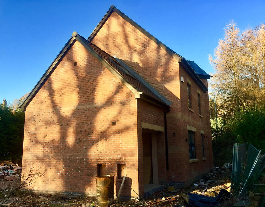 Modern two storey red brick house extension with dramatic tree shadows cast across the exterior walls