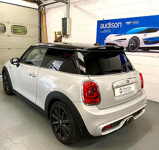 Rear view of a white Mini Hatch with a black roof and tinted windows inside a vehicle workshop
