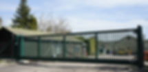A wide green security sliding gate with pointed tops protecting a commercial or industrial property