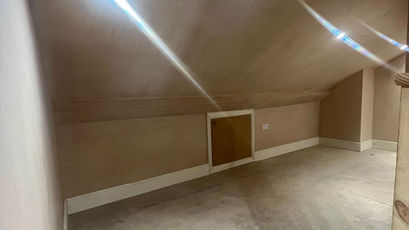 Inside a freshly plastered empty loft room with sloped ceilings and a small low-level eaves access door hatch