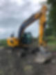 Yellow excavator on muddy ground, with overcast sky and greenery in the background