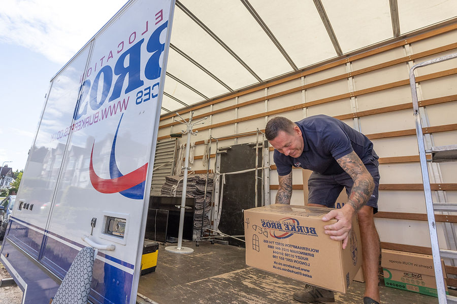 A man in a blue shirt moving a large cardboard box under a white canopy next to a branded banner