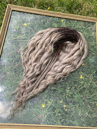 Wavy blonde and brown ombré dreadlock extensions arranged inside a gold picture frame on green grass