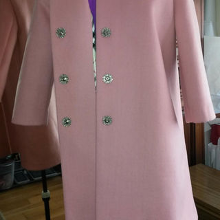 A mannequin wearing a light pink coat with shiny silver buttons