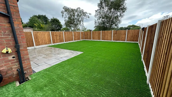 Vibrant artificial lawn framed by a stone patio and wooden perimeter fence