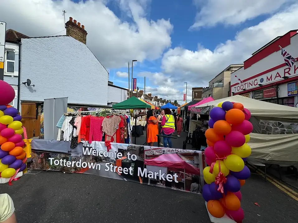 Entrance to Totterdown Street Market in Tooting with colorful balloon columns and clothing stalls