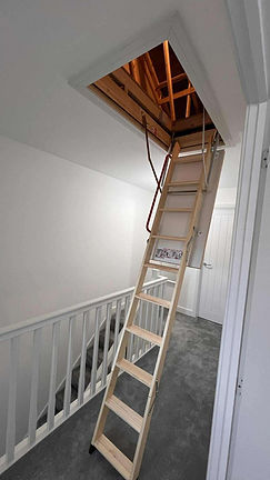 Wooden loft ladder extending from an open ceiling hatch in a bright white room