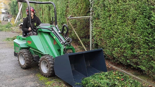 Compact green loader clearing hedge trimmings from a driveway