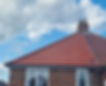 Red clay tiled roof of a brick house with a chimney against a blue sky with white clouds