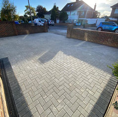 Light grey block paved driveway with a dark brick border and matching brick retaining walls under sunlight