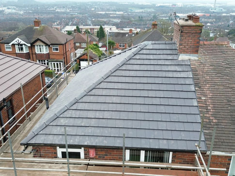 Elevated view of a grey slate hip roof with a brick chimney stack and scaffolding in a residential area