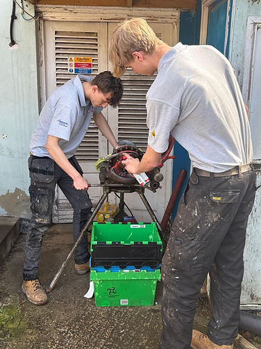Two technicians in workwear servicing a bright green industrial machine outdoors