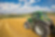 Green tractor in a harvested golden field overlooking rolling hills