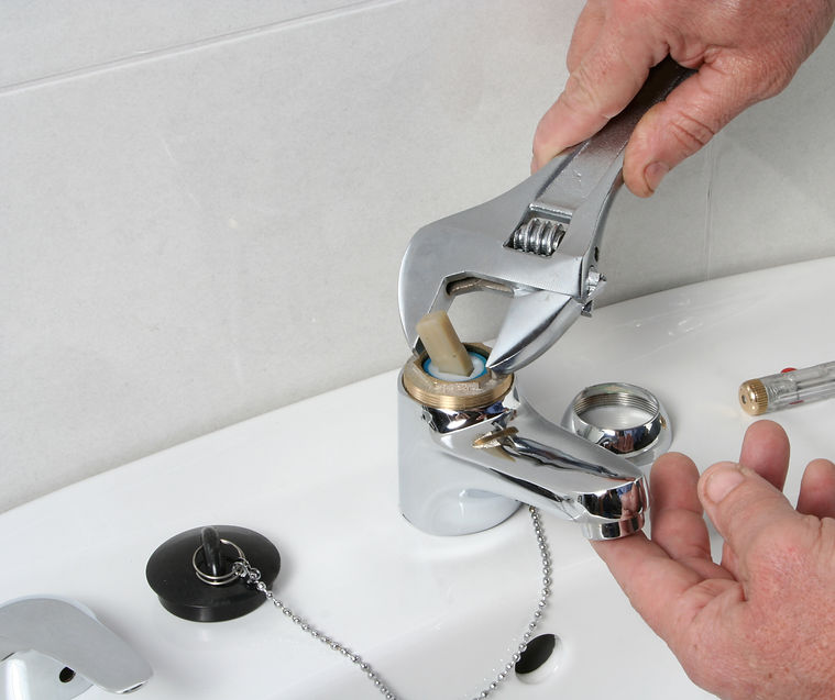 Hands using a silver adjustable spanner to dismantle the internal cartridge of a chrome bathroom tap