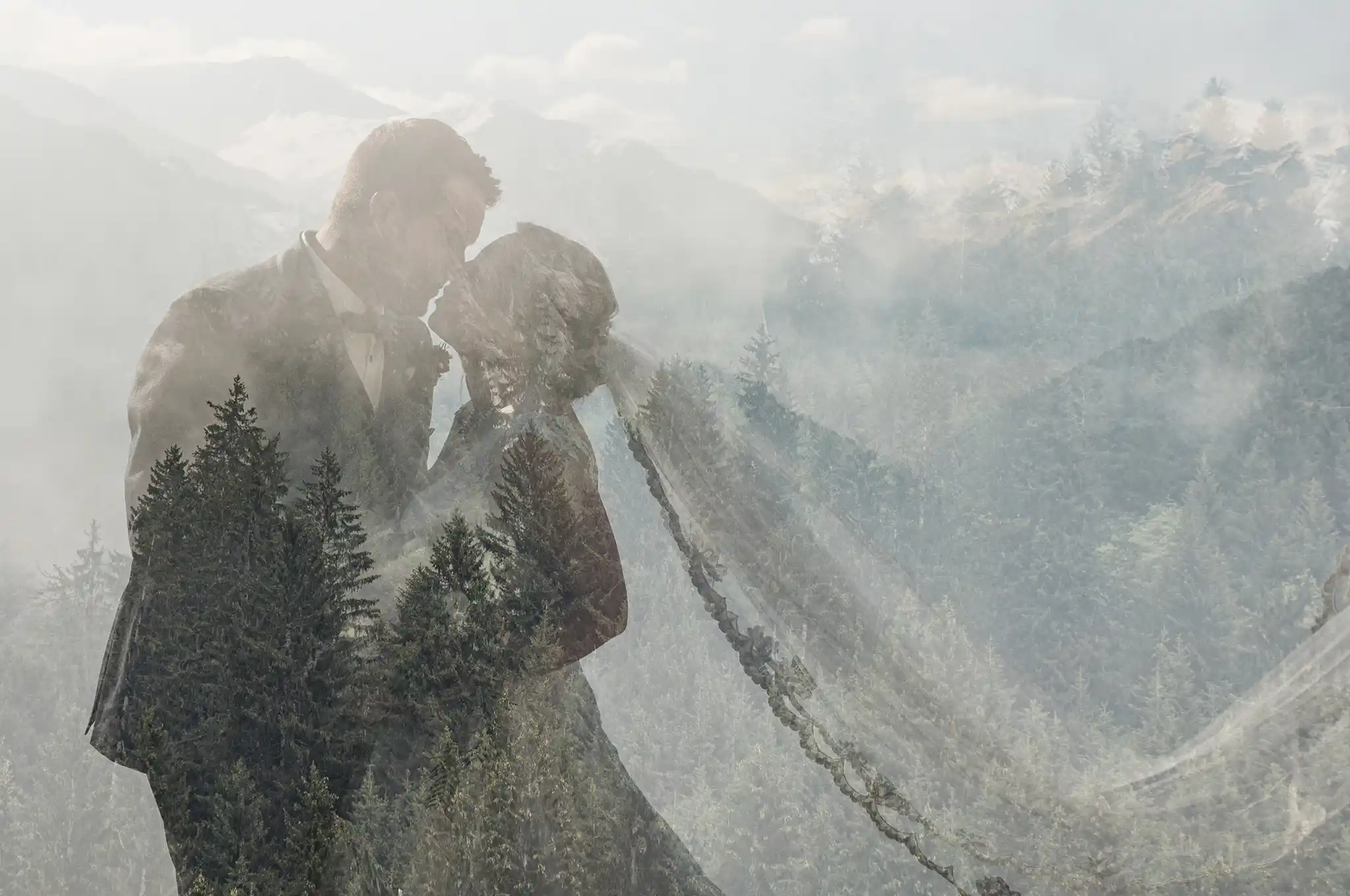 Brautpaar küsst sich vor Bergkulisse mit wehendem Schleier