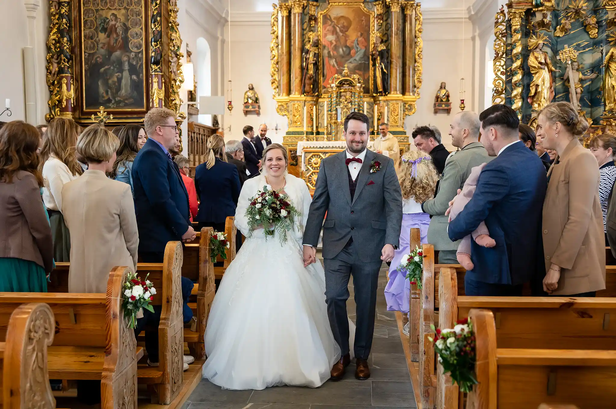 Brautpaar läuft durch den Mittelgang der katholischen Kirche in Laax, Gäste stehen in den Bänken
