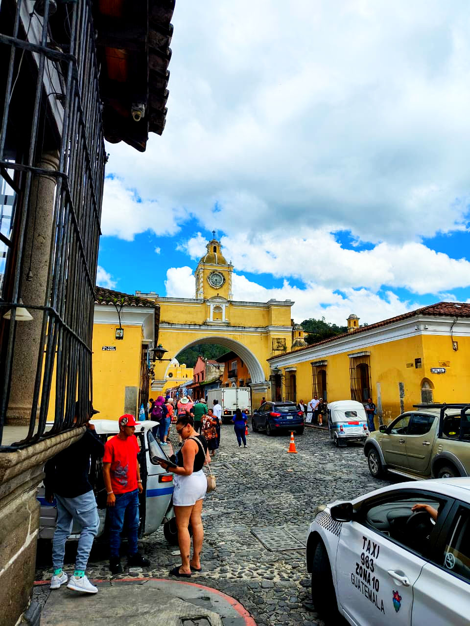 Streets of Antigua are bustling with activity under a vibrant blue sky, framed by the iconic Santa Catalina Arch.