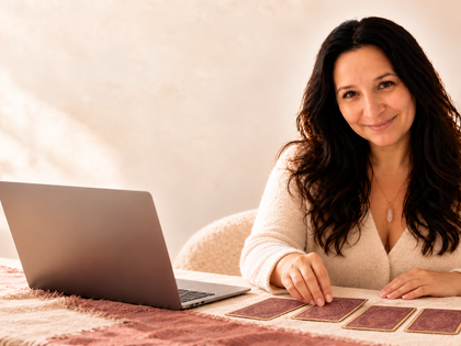 Cristina Santos at a table with Lenormand cards, a laptop and a candle during an online reading.