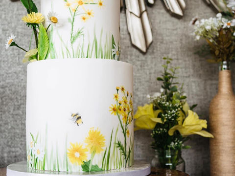 A white wedding cake with hand painted yellow flowers and bees