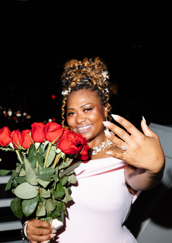 Newly engaged woman holding red roses and showing her ring