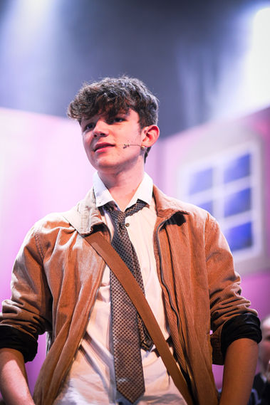 Actor in brown jacket and tie on stage